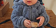 Alakai joined the competition — help win amazing prizes! baby, child, blue_onesie, fuzzy_clothing, snack, wooden_table, indoor, curious_expression, sitting, person, face, head, hands, cozy, cute, young_child, table, backpack, food, casual