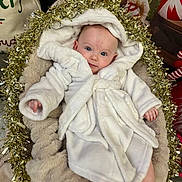 Lucia joined the competition — help win amazing prizes! baby, infant, newborn, white_robe, hood, tinsel, christmas, holiday, festive, blanket, plush_bed, cozy, portrait, blue_eyes, gaze, hands, soft_texture, indoor, cute, smile