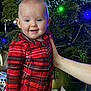 Lucia joined the competition — help win amazing prizes! baby, infant, toddler, christmas_tree, holiday, plaid, pajamas, smile, blue_eyes, chubby_cheeks, ornament, lights, present, wrapped_gift, hand, wrist_tattoo, indoor, portrait, festive, cozy