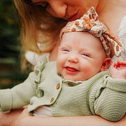 Lucia is registered to the contest to win money with this photo: baby, adult, smile, headband, knit_sweater, tattoo, arm, holding, closeup, outdoor, nature, person, happy, cute, affection, family, love, portrait, skin, flower_tattoo