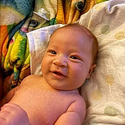 Noah is registered to the contest to win money with this photo: baby, infant, smile, face, skin, arm, blanket, colorful, soft, lying_down, cheeks, cute, newborn, expression, child, indoors, person, towel, happy, portrait