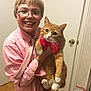 child, boy, glasses, smile, cat, orange_cat, bow_tie, pet, indoor, door, doorknob, hardwood_floor, plaid_shirt, holding, whiskers, paws, portrait, happy, home, camera