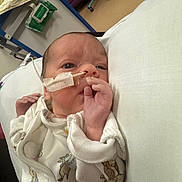 Amelia is registered to the contest to win money with this photo: newborn, baby, infant, hospital, medical_tube, feeding_tube, onesie, animal_print, lying_down, hand, face, eyes_open, healthcare, bed, blanket, patient, child, person, indoors, care