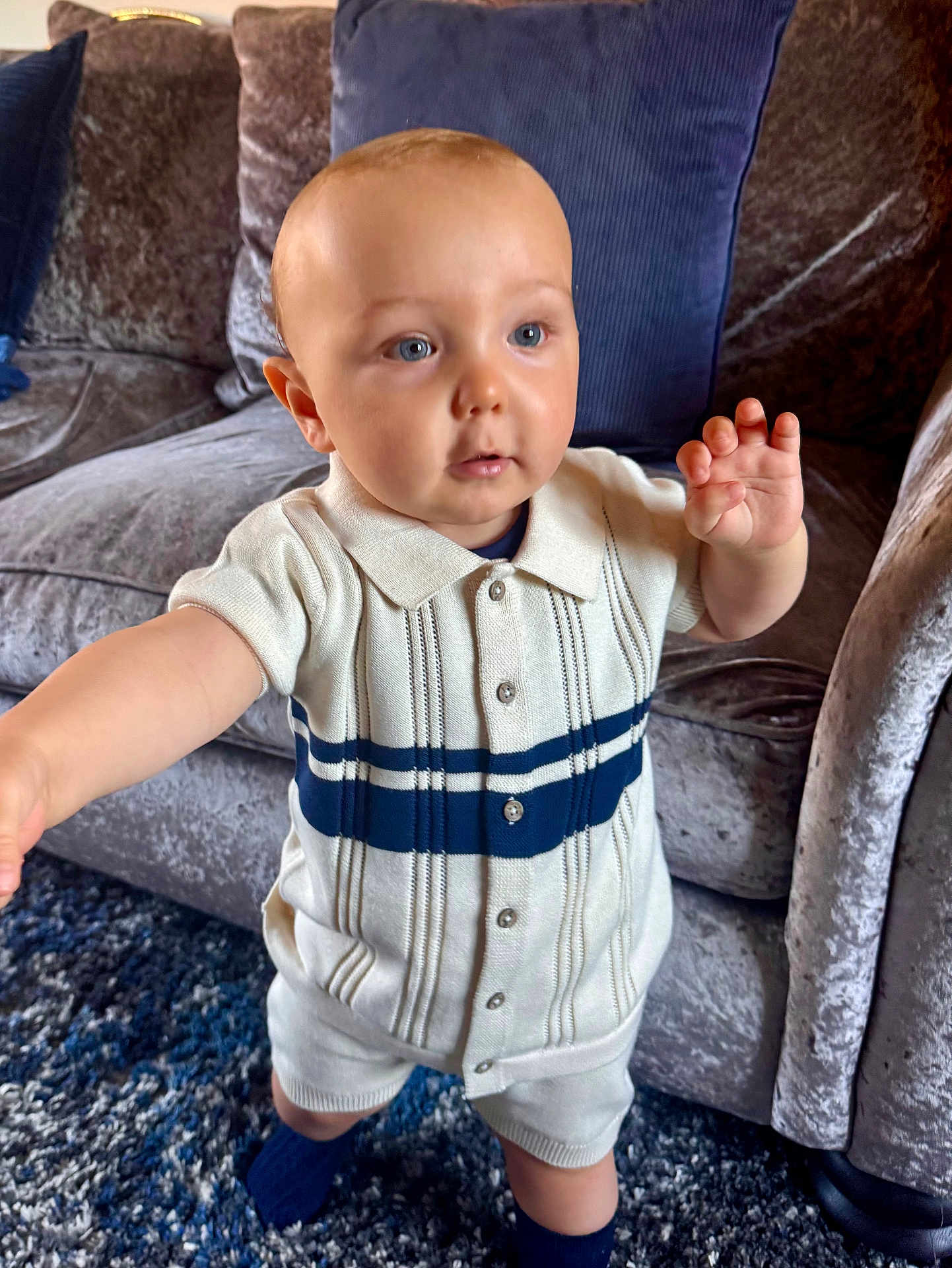 Bobby is registered to the contest to win money with this photo: baby, child, indoor, carpet, couch, velvet, furniture, clothing, socks, person, portrait, cute, standing, curious, home, blue, cream, knitwear, buttons, soft