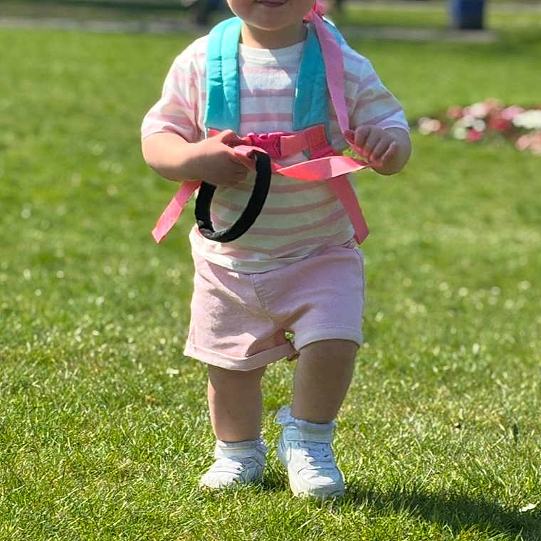 Annie-Rose is registered to the contest to win money with this photo: backpack, casual_clothing, child, cute, daylight, grass, happy, nature, outdoor, park, person, play, shirt, shoes, shorts, summer, sunlight, toddler, walking, young