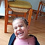 candid, casual, chair, child, expression, face, furniture, hair, happy, home, indoor, jacket, joy, laughing, person, pink_clothing, playful, seated, smiling, wooden_floor