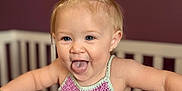 Ruth joined the competition — help win amazing prizes! toddler, child, baby, crib, bow, purple_top, smiling, tongue_out, blonde_hair, nursery, indoor, cute, happy, playful, person, furniture, wall_decor, portrait, young_child, infant