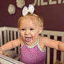 toddler, child, baby, crib, bow, purple_top, smiling, tongue_out, blonde_hair, nursery, indoor, cute, happy, playful, person, furniture, wall_decor, portrait, young_child, infant