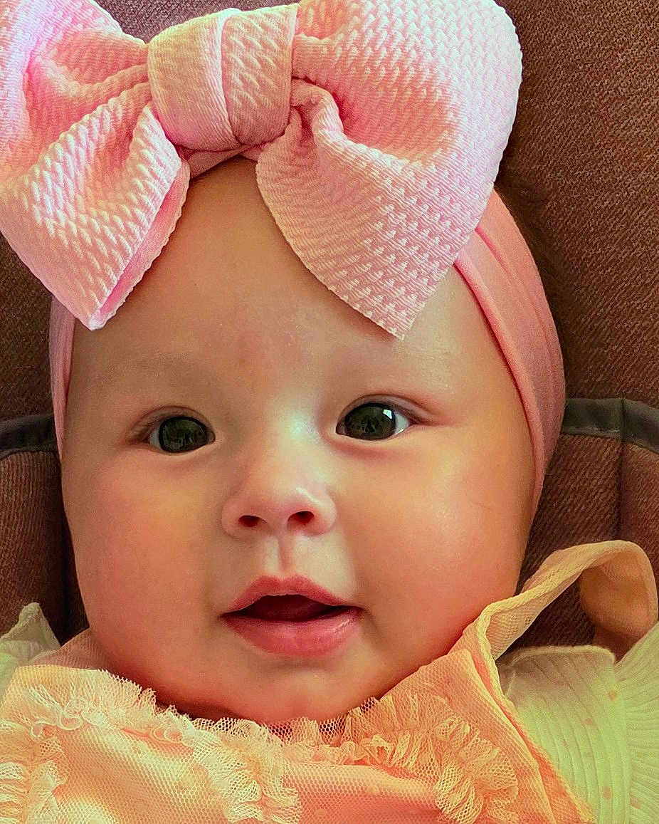 Camila joined the competition — help win amazing prizes! baby, infant, face, headband, bow, pink, peach, clothing, cute, portrait, child, young, closeup, smile, expressive_eyes, adorable, soft, texture, fabric, background