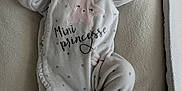 Inaya a rejoint le concours — aidez-le/la à gagner de superbes lots ! baby, newborn, sleeping, onesie, star_pattern, text_on_clothing, infant, cozy, soft_texture, cushion, resting, peaceful, cute, child, indoor, portrait, clothing, babywear, small_hands, closed_eyes