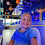 toddler, child, blue_shirt, high_chair, smiling, indoor, restaurant, space_theme, decorations, planets, lighting, happy, portrait, boy, casual_clothing, modern_interior, futuristic, seating, cute, daylight