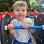 blue_bar, casual_clothing, child, cute, daylight, face, hands, happy, jeans, nature, outdoor, park, person, play_equipment, playground, seat, smile, toddler, trees, white_shirt