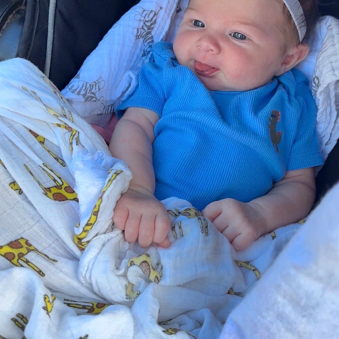 Mac is registered to the contest to win money with this photo: baby, baby_girl, blanket, blue_clothing, car_seat, child, comfort, cute, face, flower, giraffe_print, hand, headband, infant, outdoor, person, portrait, seatbelt_warning, skin, sunlight