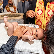 Raphaël participe au concours pour gagner de l'argent avec cette photo : baby, infant, ceremony, ritual, adult, hand, table, towel, cloth, person, religious, attire, vestments, red, gold, face, skin, indoors, celebration, people