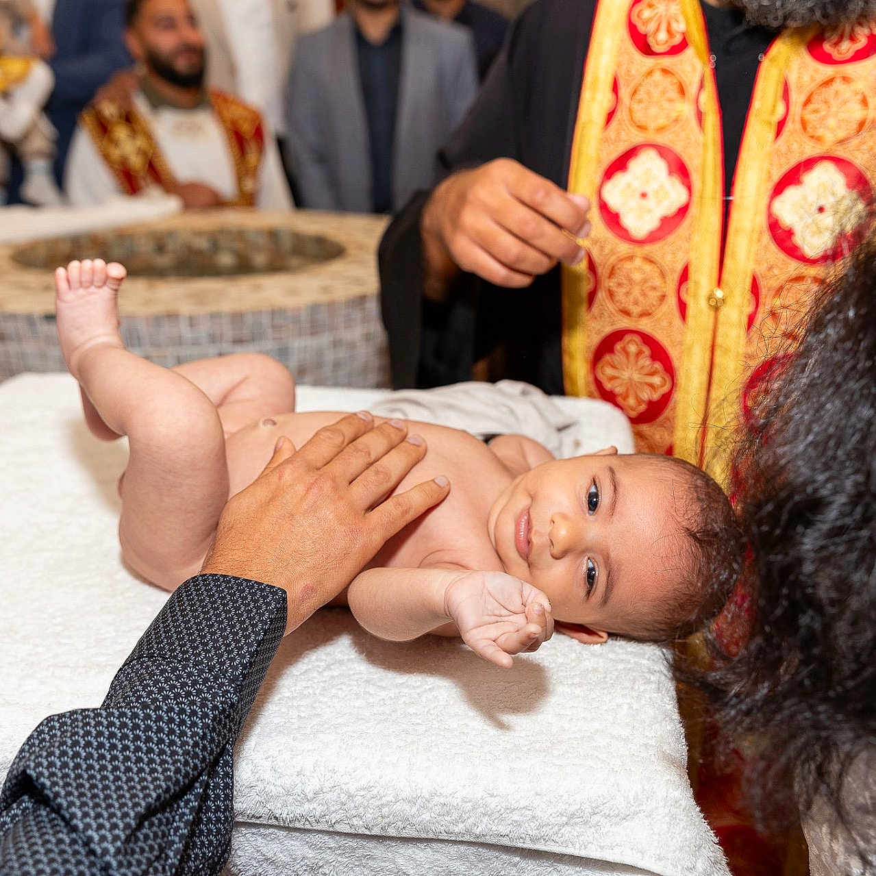 Raphaël participe au concours pour gagner de l'argent avec cette photo : adult, attire, baby, celebration, ceremony, cloth, face, gold, hand, indoors, infant, people, person, red, religious, ritual, skin, table, towel, vestments