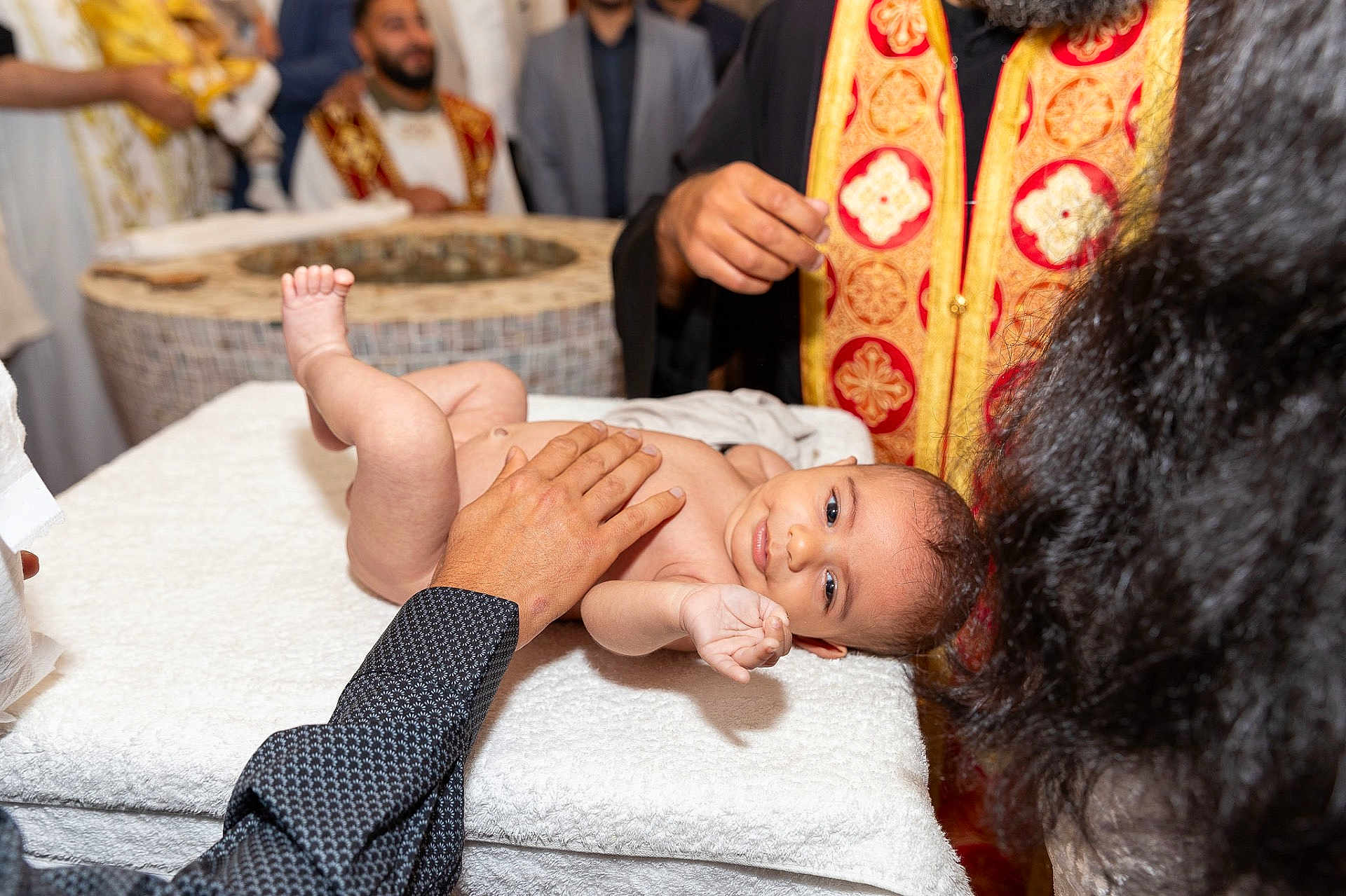 Raphaël participe au concours pour gagner de l'argent avec cette photo : baby, infant, ceremony, ritual, adult, hand, table, towel, cloth, person, religious, attire, vestments, red, gold, face, skin, indoors, celebration, people