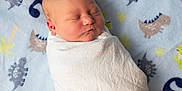 Luke is registered to the contest to win money with this photo: newborn, baby, swaddled, blanket, sleeping, infant, face, child, soft, cozy, dinosaur_pattern, blue, white, peaceful, cute, portrait, indoors, resting, toddler, fabric
