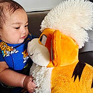 Zachary joined the competition — help win amazing prizes! baby, child, stuffed_animal, plush_toy, blue_shirt, tiger_print, indoor, couch, curious, soft_toy, cute, closeup, infant, smiling, holding, face, young, person, cozy, furniture