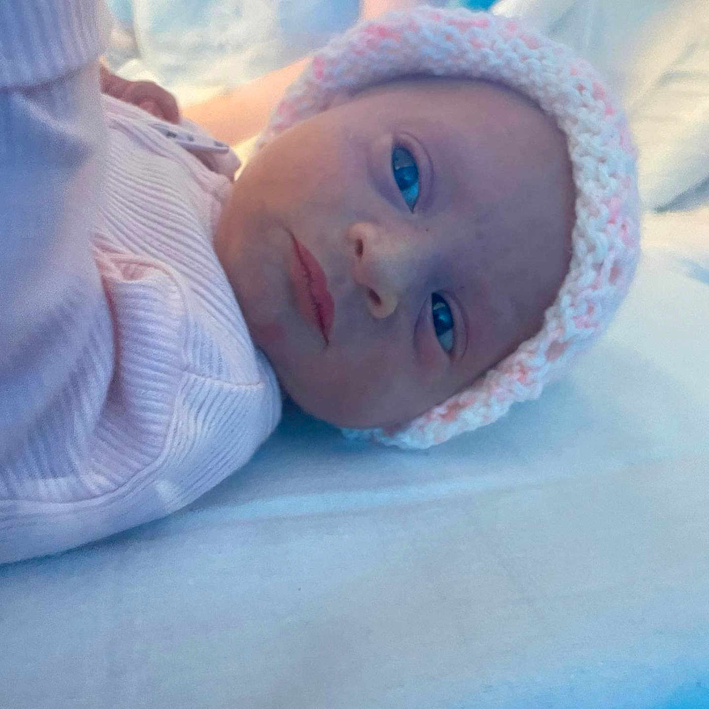 Jessie-June joined the competition — help win amazing prizes! baby, bed, blanket, blue_eyes, child, closeup, cozy, cute, face, headwear, indoors, infant, knitted_hat, lying_down, newborn, person, pink_clothing, portrait, soft_light, warm