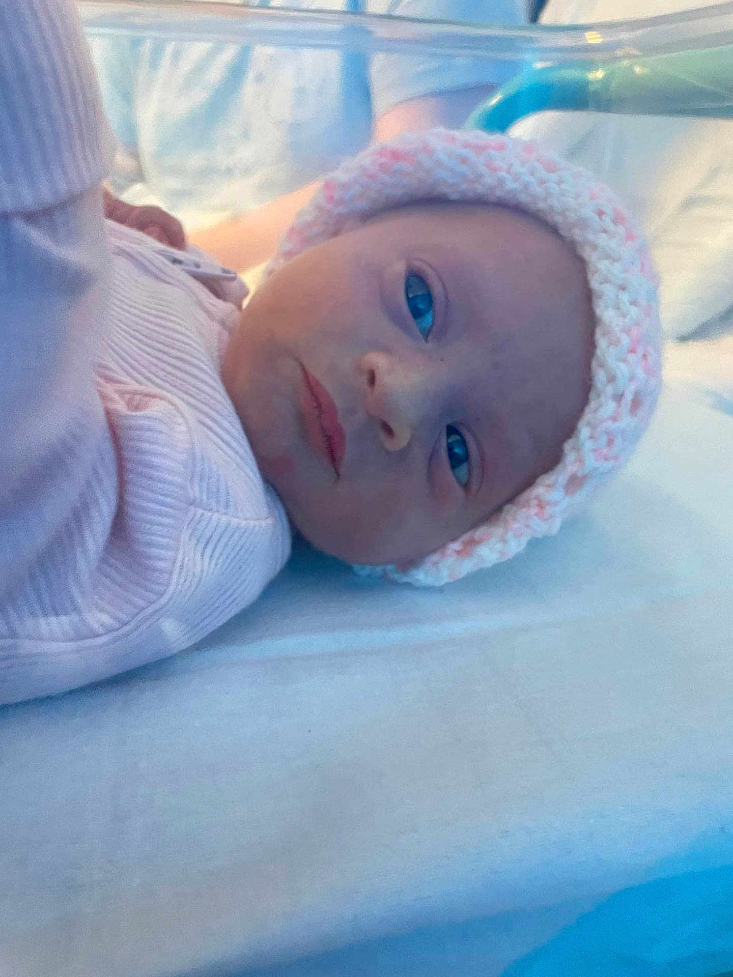 Jessie-June joined the competition — help win amazing prizes! baby, infant, knitted_hat, pink_clothing, lying_down, blue_eyes, bed, blanket, soft_light, portrait, face, newborn, cute, child, person, indoors, warm, cozy, closeup, headwear