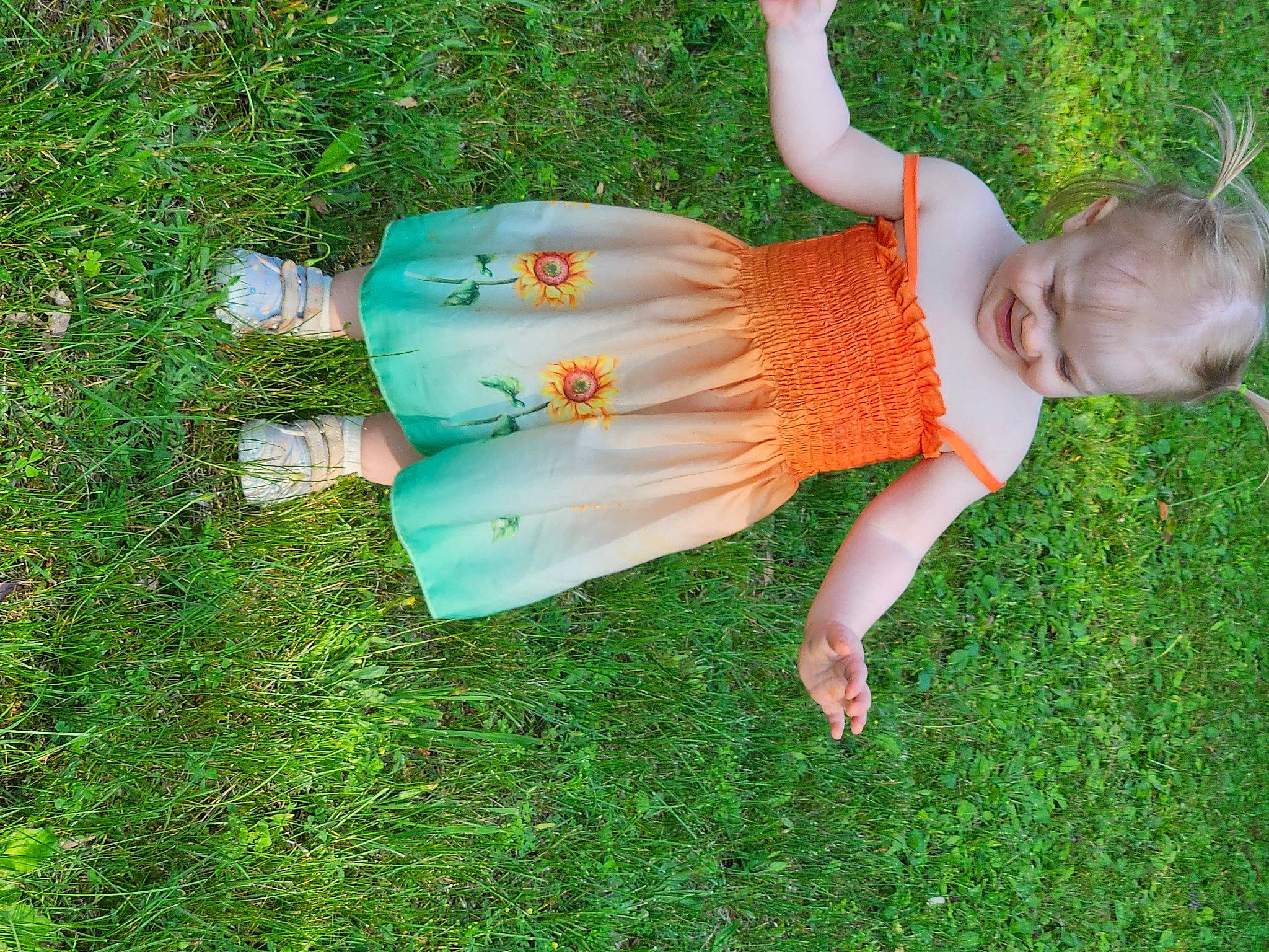 Maisy is registered to the contest to win money with this photo: baby_toddler_clothing, child, dress, foot, fun, garden, grass, grassland, green, happy, human_leg, leisure, people_in_nature, person, plant, play, sandal, shrub, sitting, toddler