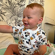 Isaac a rejoint le concours — aidez-le/la à gagner de superbes lots ! baby, child, toddler, smiling, mickey_mouse, donald_duck, pluto, tshirt, bed, blanket, wallpaper, indoor, happy, sitting, cute, person, skin, hair, face, clothing