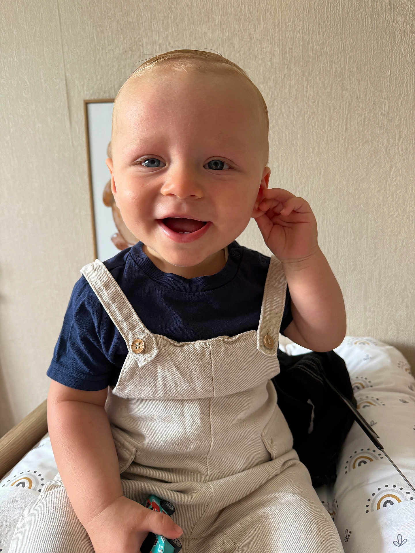 Isaac a rejoint le concours — aidez-le/la à gagner de superbes lots ! child, toddler, smiling, overalls, toy_car, blue_eyes, short_hair, sitting, indoor, cushion, patterned, navy_shirt, beige_clothing, happy, face, hand, person, playful, cute, portrait