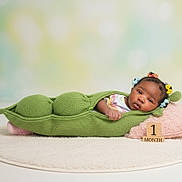 Amoura joined the competition — help win amazing prizes! baby, infant, pea_pod_costume, knitted, green, pillow, pink, hair_ties, colorful, wooden_blocks, month_marker, milestone, cute, lying_down, soft_rug, portrait, studio, child, newborn, face