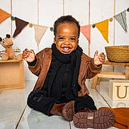 Olamilekan is registered to the contest to win money with this photo: child, toddler, smiling, brown_jacket, black_scarf, boots, floor, wooden_blocks, stuffed_animals, decorations, bunting_flags, hat, basket, indoor, happy, cute, playful, person, portrait, warm_clothing