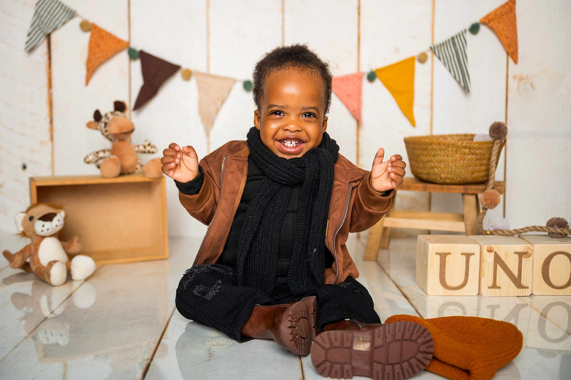 Olamilekan is registered to the contest to win money with this photo: child, toddler, smiling, brown_jacket, black_scarf, boots, floor, wooden_blocks, stuffed_animals, decorations, bunting_flags, hat, basket, indoor, happy, cute, playful, person, portrait, warm_clothing