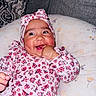 Dayani is registered to the contest to win money with this photo: baby, child, infant, smiling, happy, portrait, floral_outfit, headband, pink_clothing, cushion, pillow, indoor, sitting, lying_down, hand, fist, self_soothing, face, close_up, patterned_background