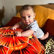 Pablo a rejoint le concours — aidez-le/la à gagner de superbes lots ! baby, infant, pillow, orange, pattern, cushion, bed, blanket, indoors, person, cute, child, smiling, face, eyes, toddler, clothing, soft, comfort, home