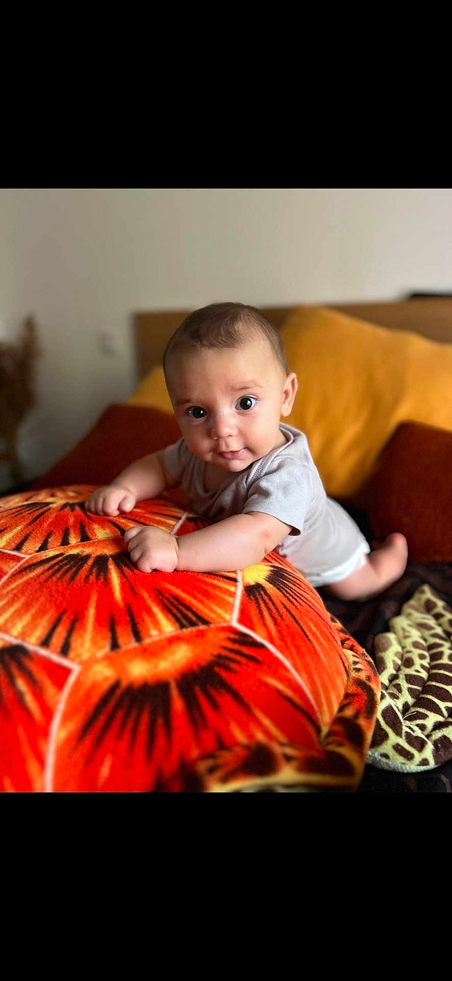 Pablo a rejoint le concours — aidez-le/la à gagner de superbes lots ! baby, infant, pillow, orange, pattern, cushion, bed, blanket, indoors, person, cute, child, smiling, face, eyes, toddler, clothing, soft, comfort, home