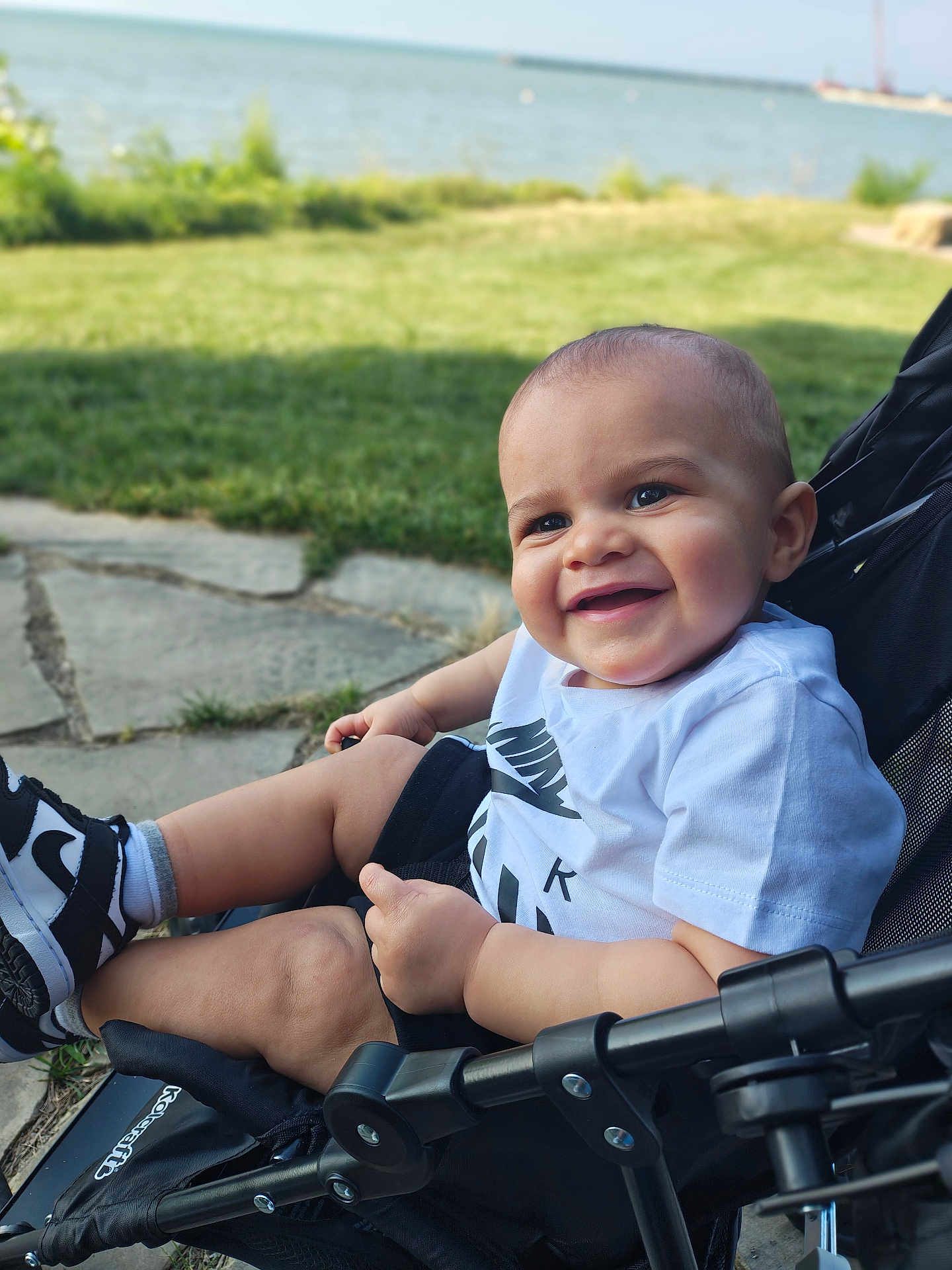 Aire joined the competition — help win amazing prizes! baby, child, smiling, stroller, outdoor, waterfront, grass, pavement, sneakers, black_and_white, happy, cute, person, summer, nature, casual_clothing, sunlight, face, head, legs