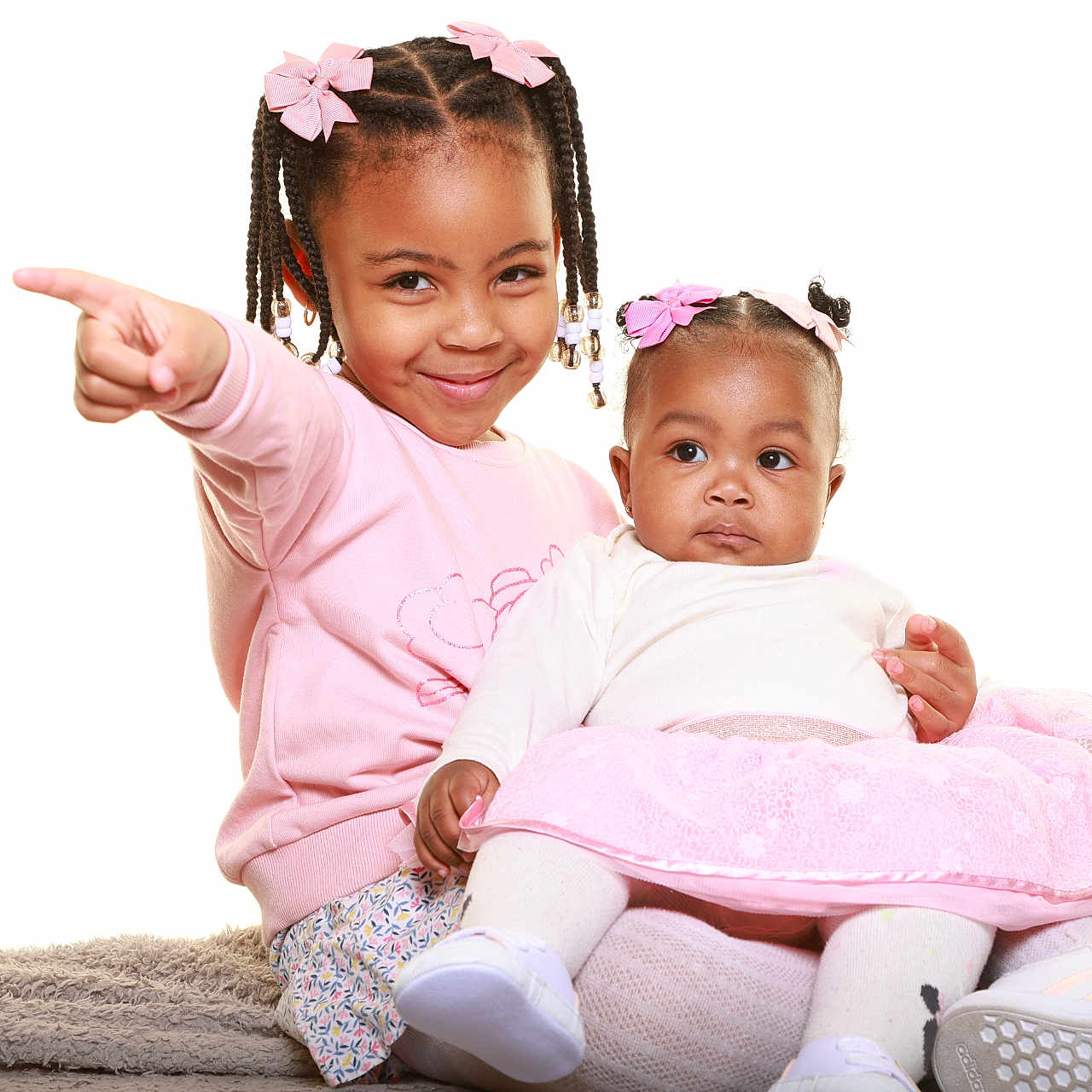 Elywen Et élohanne a rejoint le concours — aidez-le/la à gagner de superbes lots ! baby, braided_hair, child, cute, family, hair_bows, happy, indoor, infant, pink_clothing, pointing, portrait, seated, shoes, sisters, skirt, smiling, toddler, together, white_background