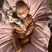 Kara a rejoint le concours — aidez-le/la à gagner de superbes lots ! baby, pacifier, plush_toy, bunny, blanket, brown_clothing, infant, soft_texture, cute, child, sleepwear, comfort, resting, indoors, pink, cozy, small_hands, portrait, relaxation, cuteness