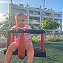 Hana participe au concours pour gagner de l'argent avec cette photo : baby, child, swing, playground, outdoor, sunlight, building, residential, fence, trees, greenery, clothing, pink_shirt, pink_shorts, barefoot, face, legs, hands, seat, chain