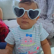 Inaya a rejoint le concours — aidez-le/la à gagner de superbes lots ! toddler, child, glasses, heart_shaped_glasses, striped_shirt, jellyfish_graphic, indoor, living_room, adult_hands, woman, hijab, sofa, couch, table, person, portrait, cute, fashion, casual, family