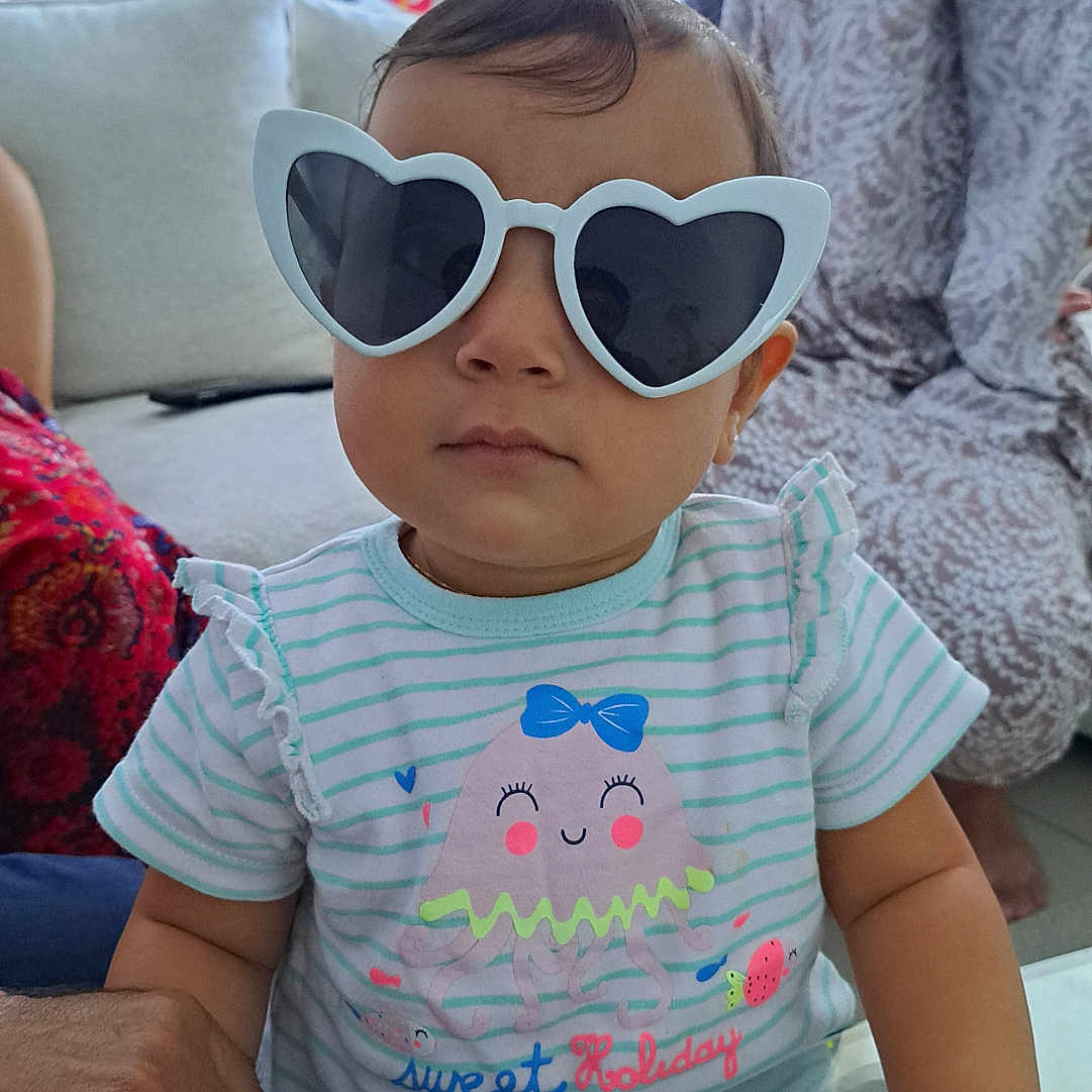 Inaya a rejoint le concours — aidez-le/la à gagner de superbes lots ! adult_hands, casual, child, couch, cute, family, fashion, glasses, heart_shaped_glasses, hijab, indoor, jellyfish_graphic, living_room, person, portrait, sofa, striped_shirt, table, toddler, woman