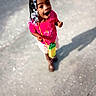 accessory, casual_clothing, child, cute, daytime, footwear, hair_beads, happy, joyful, looking_up, outdoor, pavement, person, pink_shirt, portrait, shadow, smiling, standing, sunlight, young