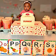 Brianna is registered to the contest to win money with this photo: alphabet_cards, baby, child, colorful, drink, dunkin, food_box, headband, indoor, milkshake, orange, pineapple, pink_clothing, portrait, queen, rabbit, smiling, sun, table, turtle