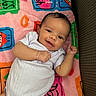 baby, smiling, infant, blanket, colorful, happy, lying_down, cute, child, person, white_clothing, indoors, soft_texture, playful, face, young, toddler, cozy, cheerful, portrait