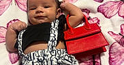 Sariah joined the competition — help win amazing prizes! accessory, baby, black_top, blanket, butterfly_pattern, child, clothing, cute, fashion, handbag, indoors, infant, lying_down, patterned_shorts, person, portrait, red_handbag, smiling, soft_texture, white_shorts