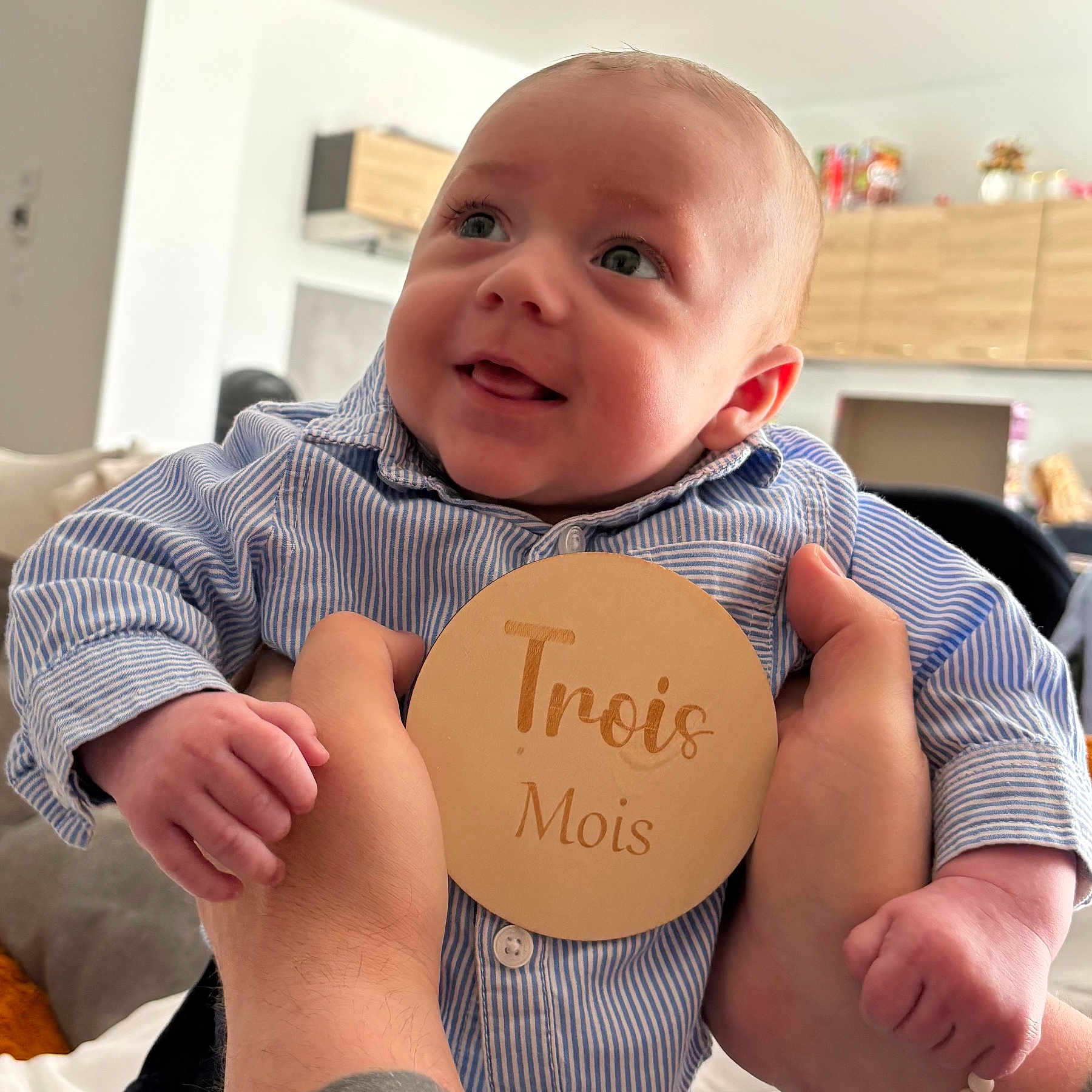 Elyaz a rejoint le concours — aidez-le/la à gagner de superbes lots ! baby, infant, child, smiling, blue_shirt, striped_clothing, hands, wooden_sign, text, indoor, home, couch, person, portrait, cute, happy, skin, face, eyes, tongue