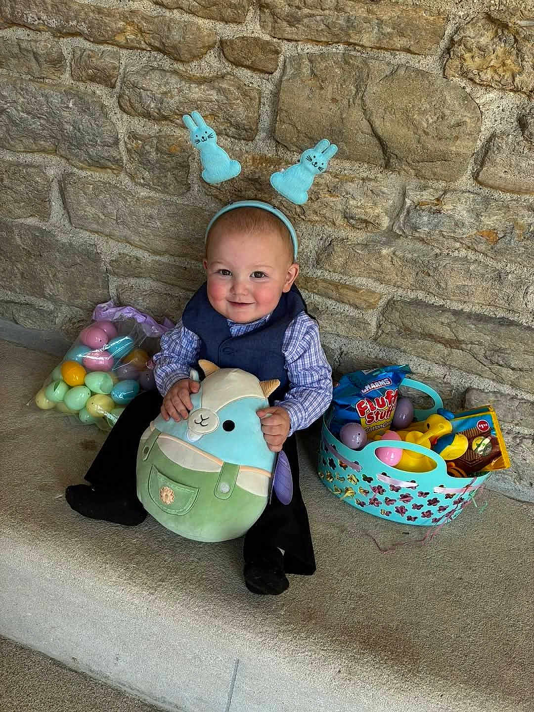 Grayson is registered to the contest to win money with this photo: toddler, child, bunny_ears, stuffed_animal, easter_eggs, basket, candy, toy, stone_wall, bench, smiling, cute, indoors, plush, clothing, headband, happy, sitting, holiday, celebration