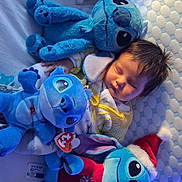 Nyara a rejoint le concours — aidez-le/la à gagner de superbes lots ! baby, sleeping, plush_toy, stuffed_animal, stitch, bed, pillow, blanket, soft_toy, child, cute, indoor, holiday, christmas_hat, cozy, resting, blue_tone, toy, bedroom, infant