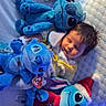 baby, sleeping, plush_toy, stuffed_animal, stitch, bed, pillow, blanket, soft_toy, child, cute, indoor, holiday, christmas_hat, cozy, resting, blue_tone, toy, bedroom, infant