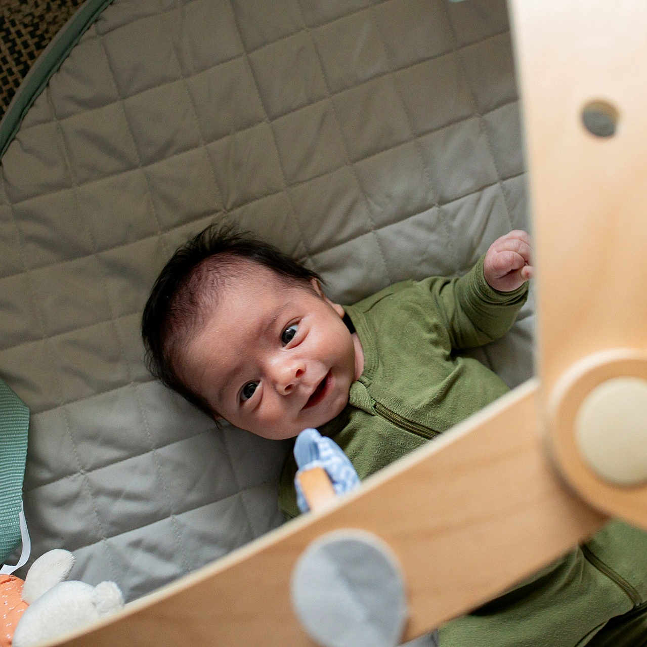 Lashaun is registered to the contest to win money with this photo: baby, baby_toys, child, close_up, cute, face, floor_mat, green_onesie, happy, head, indoors, infant, lying_down, person, playtime, quilted_mat, smiling, soft_toy, wooden_baby_gym, wooden_toy