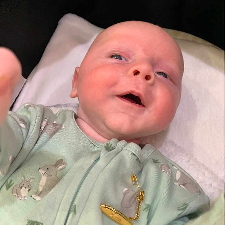 Koa is registered to the contest to win money with this photo: baby, blanket, bunny_prints, child, clothing, cute, face, gold_pin, hand, head, indoors, infant, lying_down, newborn, onesie, person, portrait, skin, smiling, soft