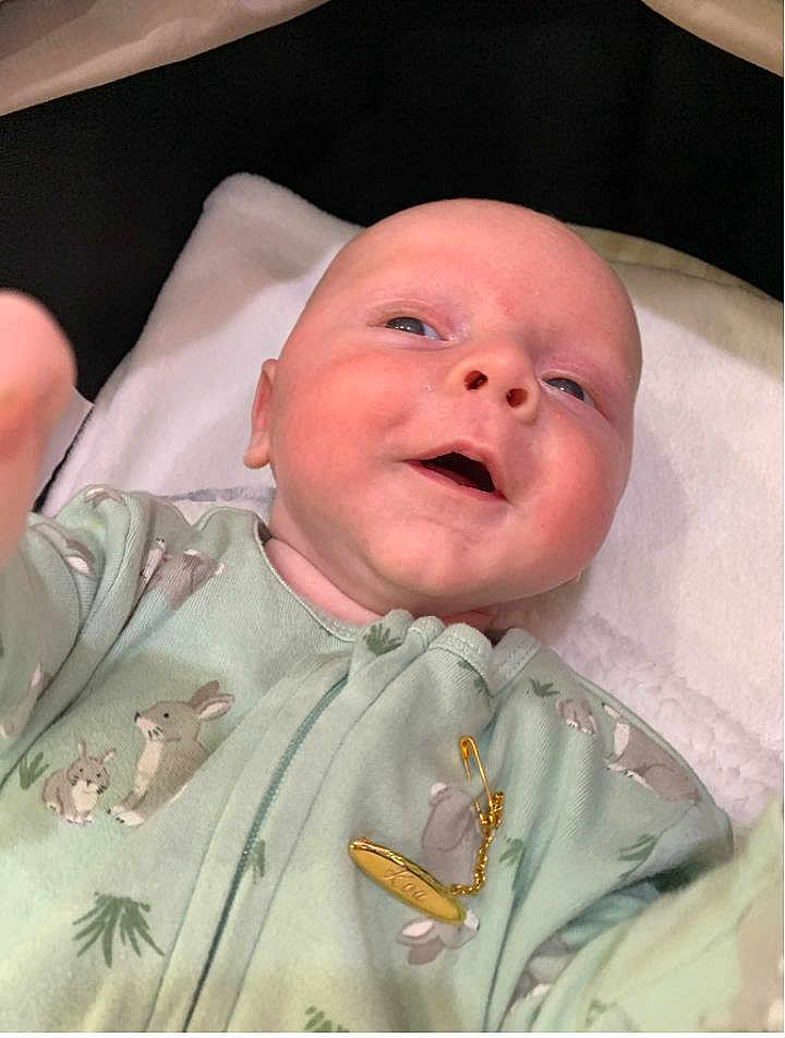 Koa is registered to the contest to win money with this photo: baby, infant, smiling, onesie, bunny_prints, blanket, soft, cute, hand, face, head, skin, lying_down, clothing, gold_pin, indoors, child, person, newborn, portrait